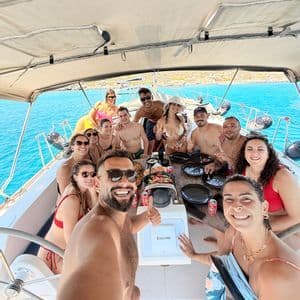 Un viaggio di gruppo WeRoad si scatta un selfie su una barca a vela, riuniti intorno a un tavolo con cibo e bevande in mare aperto.