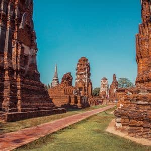 Ein Ziegelweg führt durch eine Anlage aus alten roten Ziegeltempelruinen und Stupas unter klarem blauem Himmel.
