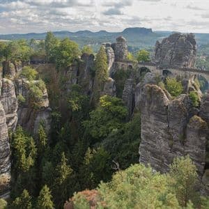 Eine lange Steinbrücke mit Bögen überquert ein von hohen, baumbewachsenen Felsformationen umgebenes Gebirgstal.