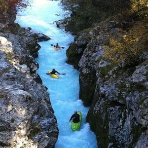 Eine WeRoad-Gruppe paddelt auf einem leuchtend blauen Fluss, der sich aus der Vogelperspektive durch eine enge, felsige Schlucht schlängelt.