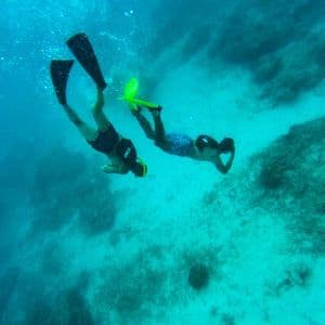 A WeRoad group trip with two people snorkeling in turquoise water above a rocky seafloor.