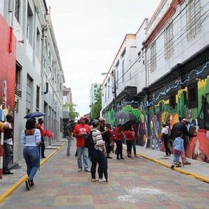 Un grupo de personas se encuentra en una calle estrecha y pavimentada, observando murales coloridos que cubren los lados de los edificios.