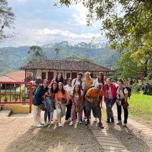 Un viaje en grupo de WeRoad posa para una foto en un sendero frente a un edificio rural, con exuberantes colinas verdes de fondo.
