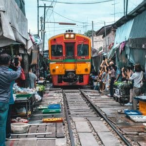 Un treno arancione e rosso si avvicina sui binari che attraversano un mercato affollato mentre le persone si spostano per scattare foto.
