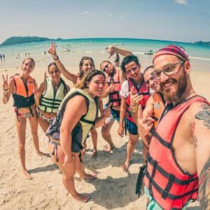 Eine WeRoad-Gruppe macht mit Schwimmwesten ein lächelndes Selfie an einem sonnigen Sandstrand am Meer.