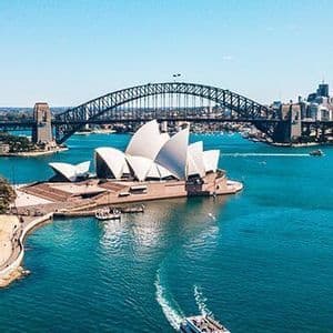 Vue aérienne de l'Opéra de Sydney et du Harbour Bridge, avec un ferry naviguant sur l'eau bleu vif en contrebas.