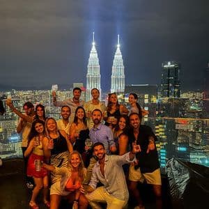 Un gruppo WeRoad posa per una foto su un tetto di notte, con torri gemelle illuminate sullo sfondo.