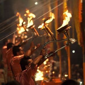 Una fila de hombres con túnicas naranjas realiza una ceremonia espiritual de noche, sosteniendo grandes lámparas llameantes.