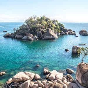 Una piccola isola rocciosa coperta di alberi si trova in acque limpide e turchesi circondata da massi.