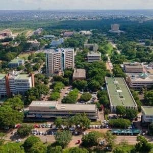 Una vista aerea di una città con edifici moderni che si ergono sopra fitti alberi verdi, con parcheggi e strade visibili sotto.