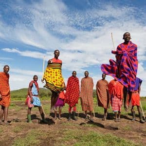 Un gruppo di Maasai in abiti tradizionali colorati in un campo, con due uomini che saltano in alto.