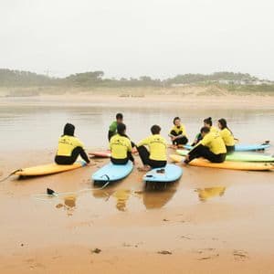Un grupo de WeRoad con camisetas amarillas se sienta en tablas de surf en círculo en una playa para una clase de surf.