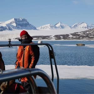Una persona con chaqueta naranja y gorro rojo en un barco durante un viaje en grupo de WeRoad, con montañas nevadas y hielo en el agua.