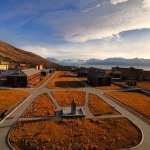 Una vista aérea de un pueblo ártico con edificios y carreteras, situado junto a una montaña, con un fiordo y glaciares al fondo.