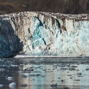 Un gran muro glaciar de hielo azul y blanco se alza sobre aguas oscuras, con pequeños icebergs flotando.