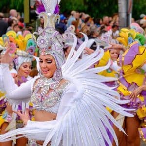 Una donna in un costume di carnevale bianco e ingioiellato con piume balla durante una sfilata di strada con altri artisti.