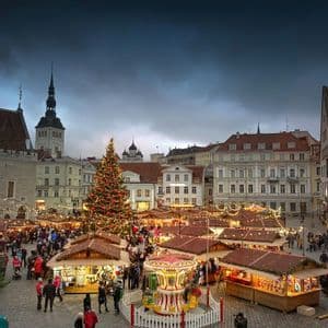 Un vivace mercatino di Natale in una piazza acciottolata con un grande albero di Natale illuminato, bancarelle e una giostra.
