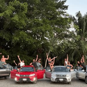 Un gruppo WeRoad in viaggio, con persone in posa su e intorno a quattro SUV parcheggiati davanti a rigogliosi alberi verdi.