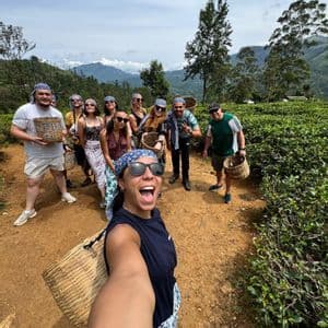 Un groupe WeRoad pose pour un selfie sur un sentier dans une plantation de thé, tenant des paniers tressés pour la cueillette du thé.