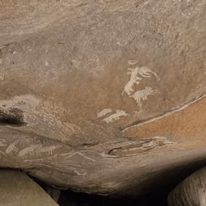 Antica arte rupestre con dipinti bianchi e rossi di animali sotto un grande strapiombo roccioso piatto.