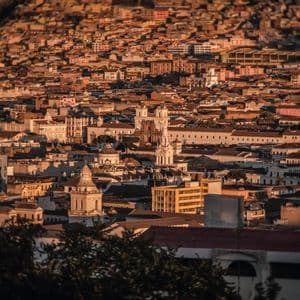 Un vasto paesaggio urbano di edifici storici e tetti in tegole che si estende su una collina al tramonto.