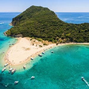 Veduta aerea di un'isola verde lussureggiante con una lingua di sabbia dove numerose barche sono ormeggiate in acque turchesi vicino alla costa.