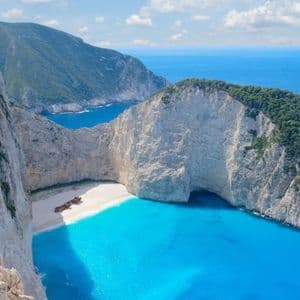 Un relitto arrugginito su una spiaggia isolata di sabbia bianca, circondata da alte scogliere bianche e acque turchesi.
