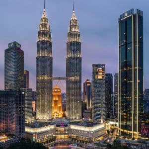 Les Tours Petronas illuminées et les gratte-ciel environnants composent une ligne d'horizon urbaine moderne au crépuscule, avec une fontaine colorée en contrebas.