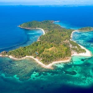 Una vista aerea di un'isola tropicale lussureggiante e verde con spiagge di sabbia bianca, circondata da acque limpide turchesi e blu intenso.