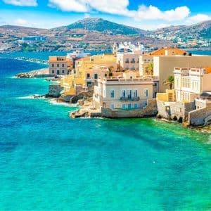Una città costiera con edifici gialli e bianchi si trova su una costa rocciosa accanto a un mare turchese sotto un cielo blu e parzialmente nuvoloso.