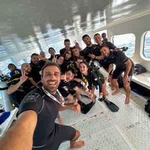 Eine WeRoad-Gruppenreise in Tauchausrüstung posiert für ein Gruppenselfie an Bord eines Bootes.