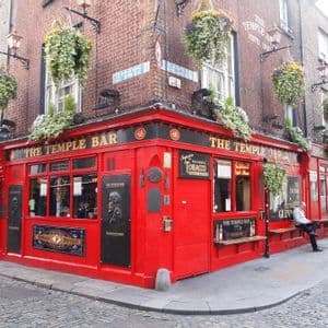La facciata rosso brillante del pub The Temple Bar su un angolo di strada acciottolata, ornata da cesti di fiori appesi.