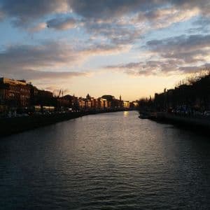Un ampio fiume scorre attraverso una città al tramonto, con edifici che costeggiano le sponde sotto un cielo nuvoloso.