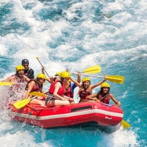 Eine WeRoad-Gruppe jubelt beim Wildwasser-Rafting in einem roten Schlauchboot auf unruhigem blauen Wasser.