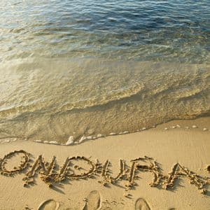 Das Wort Honduras ist in den Sand am Strand geschrieben, während sanftes Meerwasser ans Ufer gespült wird.