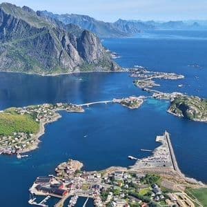 An aerial view of a coastal village built across several small islands connected by bridges, with a mountain range in the background.