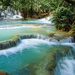 Foto a lunga esposizione di cascate a gradoni con acqua turchese in una giungla lussureggiante.