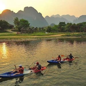 Un viaggio di gruppo WeRoad in kayak su un fiume tranquillo al tramonto, con grandi montagne stagliate sullo sfondo.