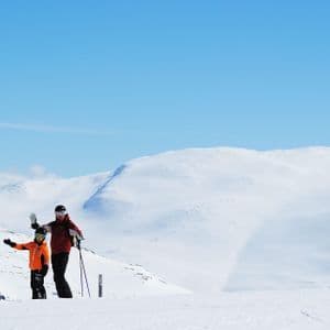 Due persone di un gruppo WeRoad in tenuta da sci che salutano su una montagna innevata sotto un cielo azzurro.