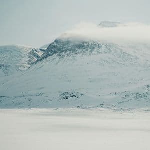 Una catena montuosa innevata con le sue cime avvolte dalle nuvole sotto un cielo pallido e coperto.