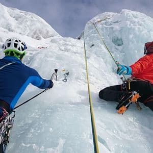 Due alpinisti di un gruppo WeRoad scalano una ripida parete di ghiaccio con corde e attrezzatura completa da arrampicata.