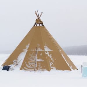 Una grande tenda teepee color sabbia si erge in un paesaggio innevato con pale e blocchi di ghiaccio nelle vicinanze sotto un cielo grigio.