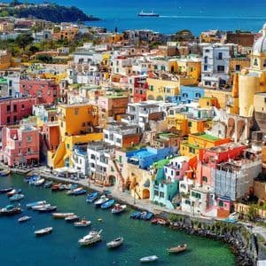 A high-angle view of a colorful coastal town with buildings packed onto a cliffside overlooking a harbor full of boats.