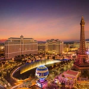 Un horizonte urbano iluminado con una réplica de la Torre Eiffel, edificios de hoteles y fuentes al atardecer