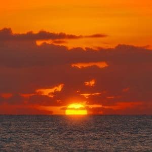 Le soleil jaune se couche sur l'horizon de l'océan sous un ciel orange vif rempli de nuages sombres.