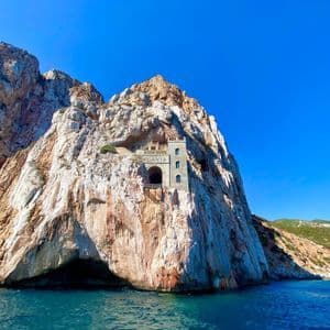 The Porto Flavia mining port, a stone structure carved into a sheer sea cliff above the blue water.