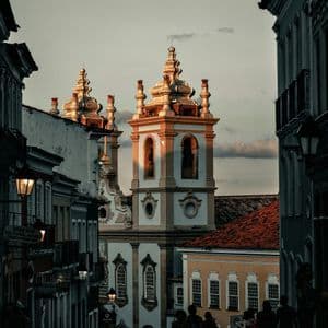 Una chiesa sontuosa con due campanili, illuminata dal tramonto, vista da una strada di ciottoli in ombra sottostante.
