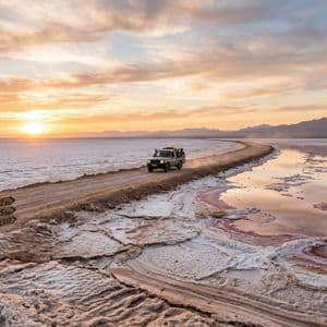 Ein Geländewagen einer WeRoad-Gruppenreise fährt bei Sonnenuntergang auf einem unbefestigten Damm über die Salzwüste Chott el Jerid.