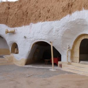 Ein weiß getünchtes Gebäude, das in einen Erdhügel gebaut ist und mehrere gewölbte Türen sowie einen Innenhof aufweist.