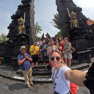 Un viaje en grupo de WeRoad posa para una selfie con un guía, haciendo un gesto de oración frente a una tradicional puerta de piedra negra.